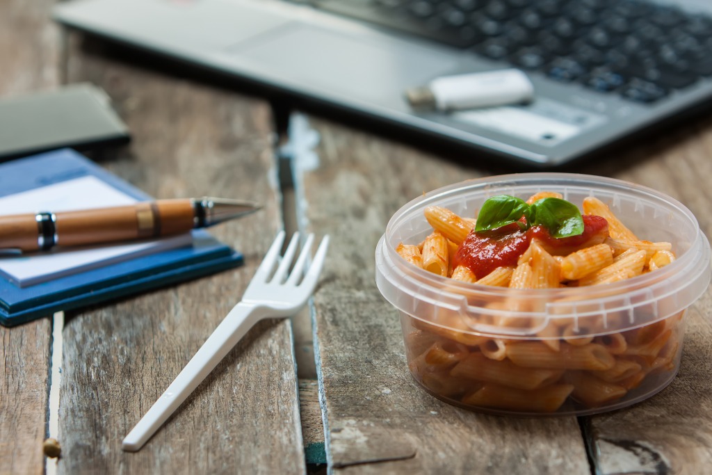 Packed lunch of pasta near a laptop