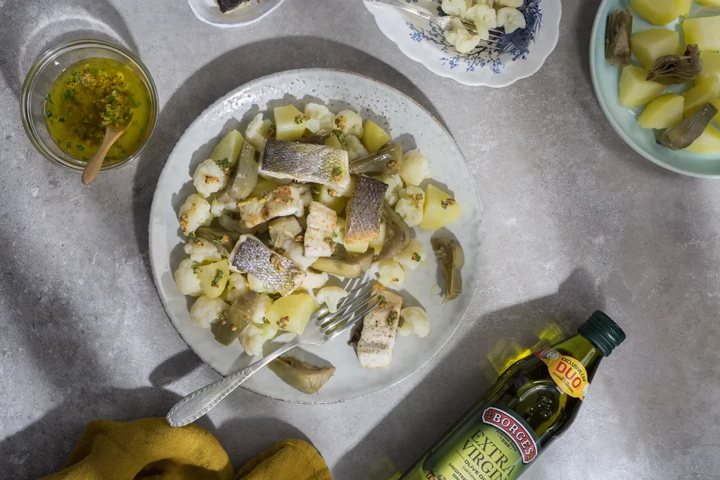 Lubina sobre una base de ensalada de alcachofa y coliflor servida con aliño de aceite de oliva y especias