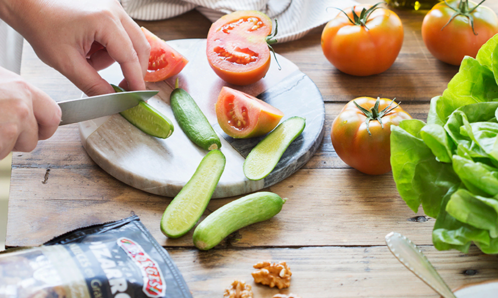 Manos cortando pepinos y tomates para preparar una ensalada saludable, imprescindible para un corazón sano
