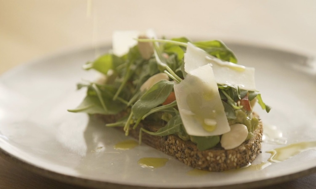Avocado, arugula and parmesan toast served in a white dish with olive oil