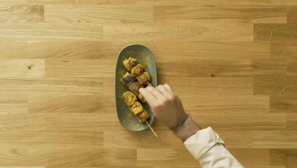 Tres brochetas de pollo con curry servidas sobre plato de cerámica