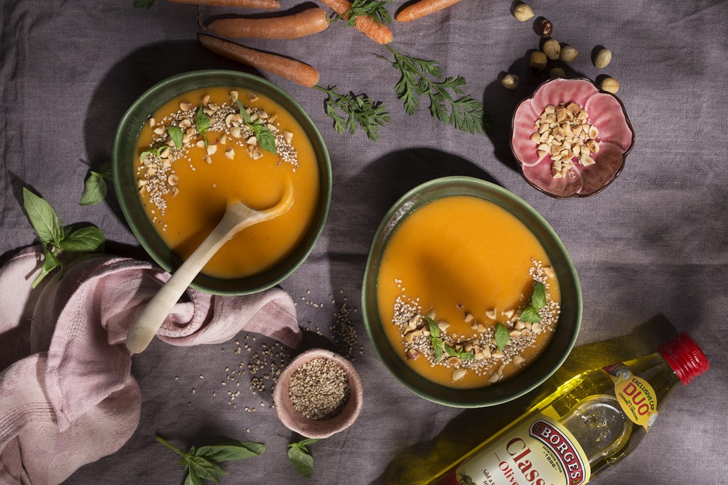 Carrot soup served in bowls with chopped hazelnuts and sesame seeds