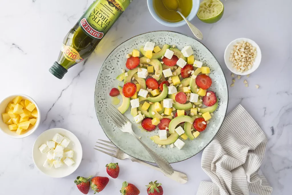 A dish of avocado salad with strawberries, cheese and mango and a bottle of olive oil