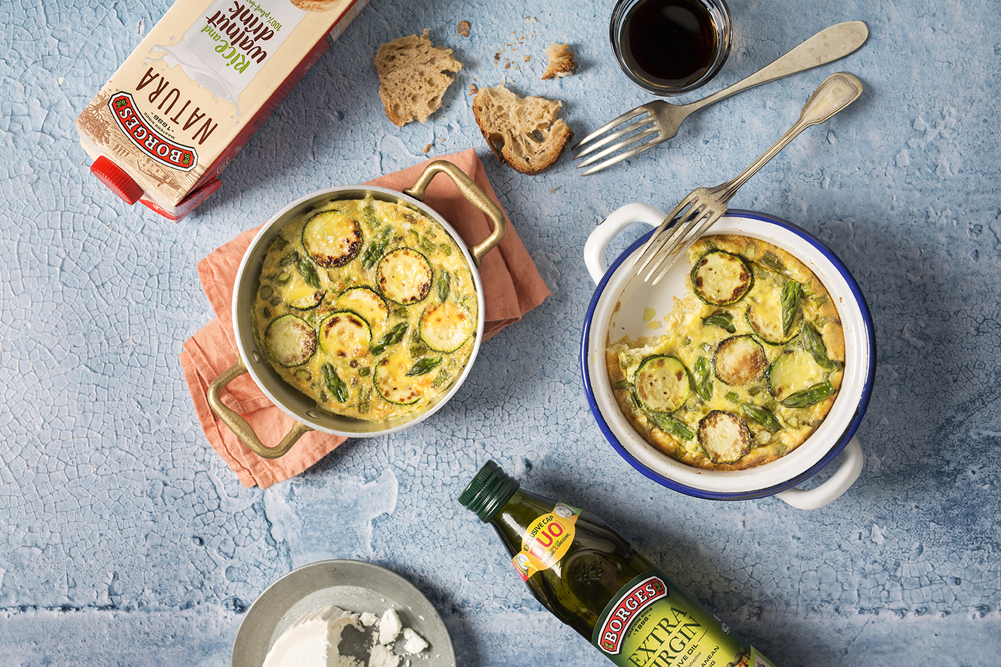 Asparagus and zucchini frittata served in two casseroles with a bottle of olive oil and nut drink