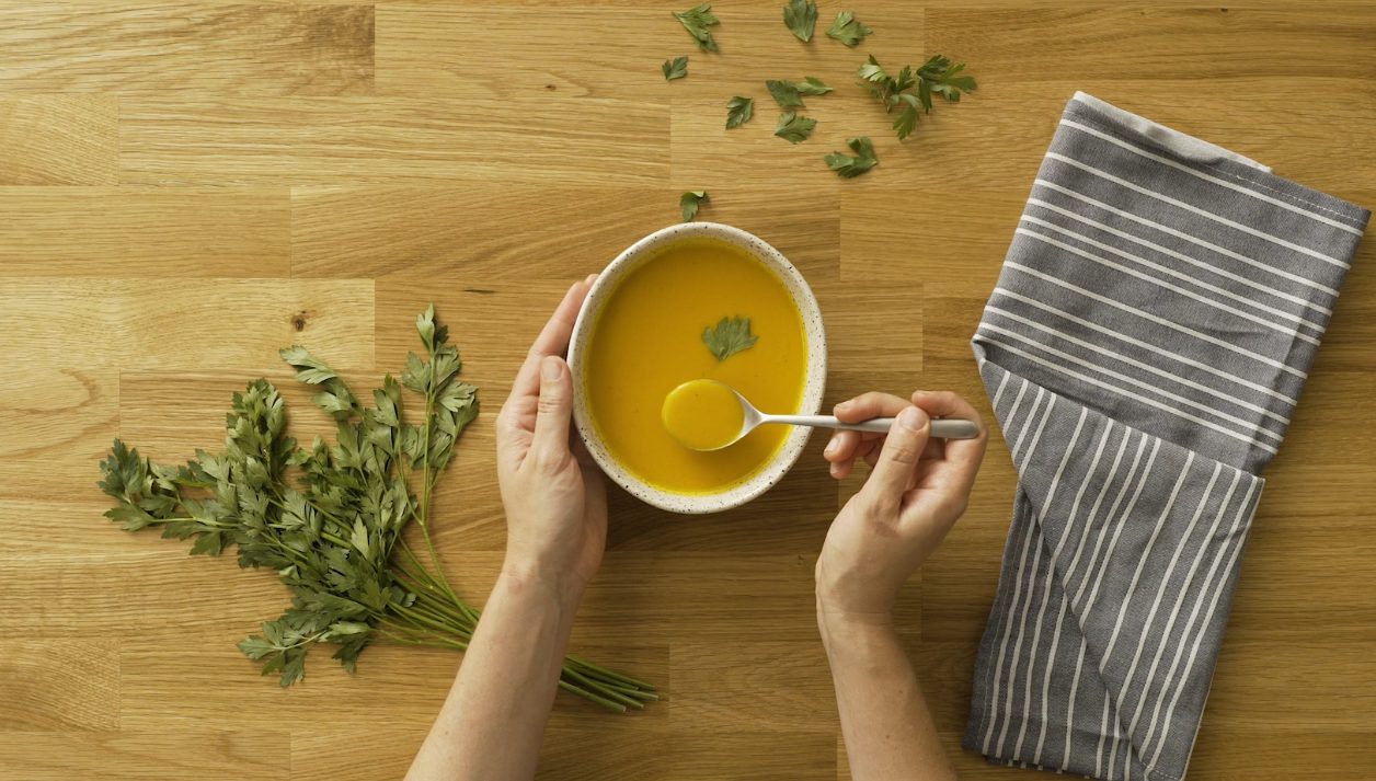 Carrot and orange creamy soup recipe served in a bowl next to a tea towel and basil